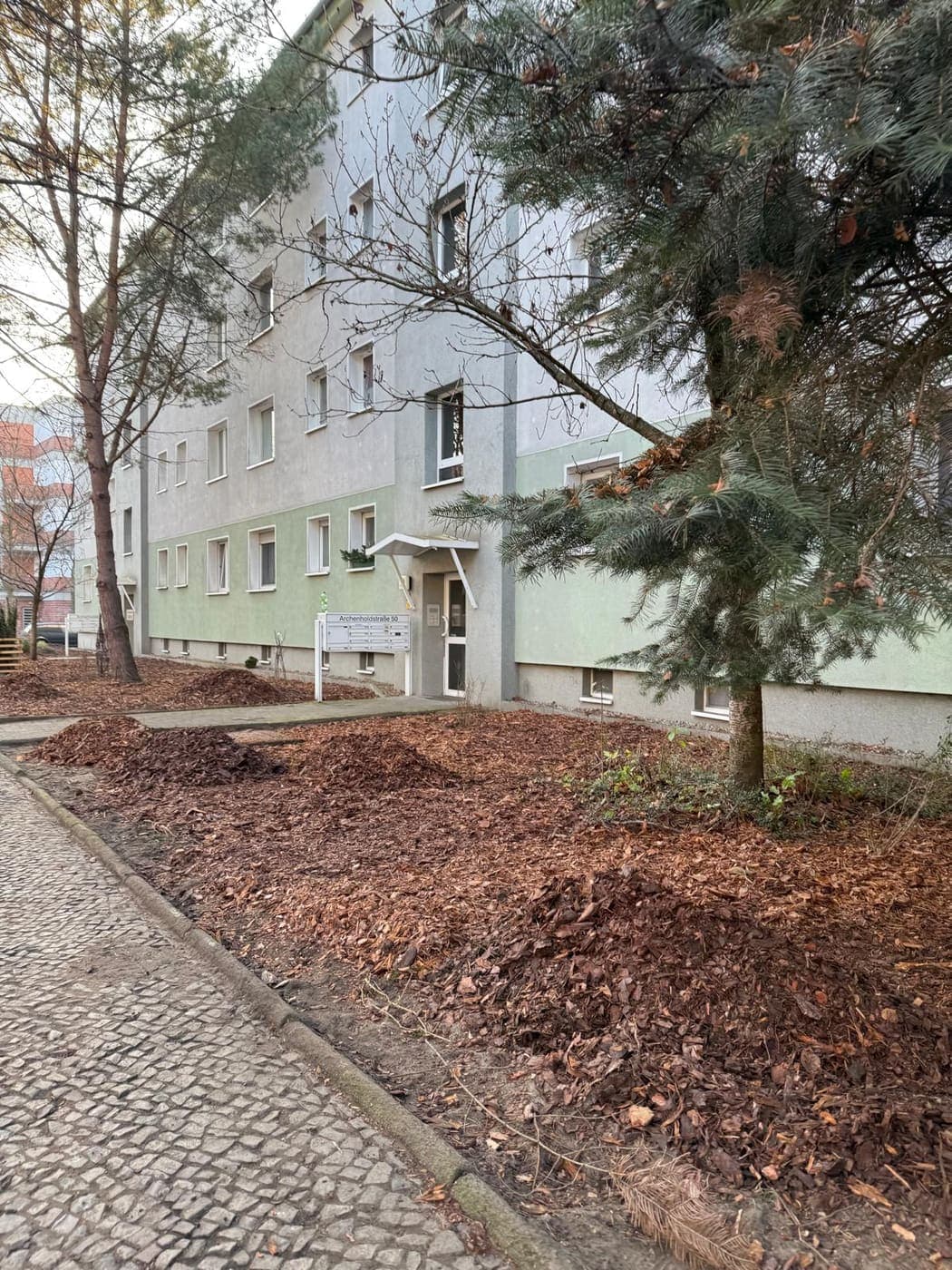 Neu angelegter, mit Rindenmulch abgedeckter Grünstreifen entlang eines Wohnblocks in der Archenholdstraße