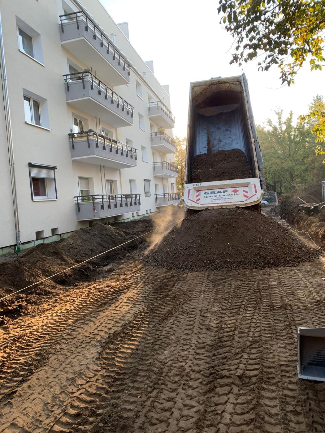 Kipplaster schüttet Mutterboden für eine neue Außenanlage vor einem Wohnhaus mit Balkonen ab
