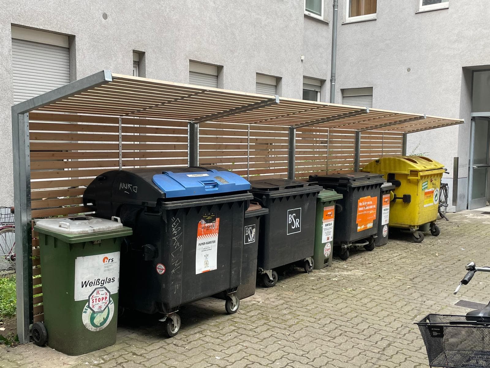 Mülltonnen-Einhausung aus Holzlatten auf Metallrahmen mit überdachtem Dach in einem Berliner Hinterhof