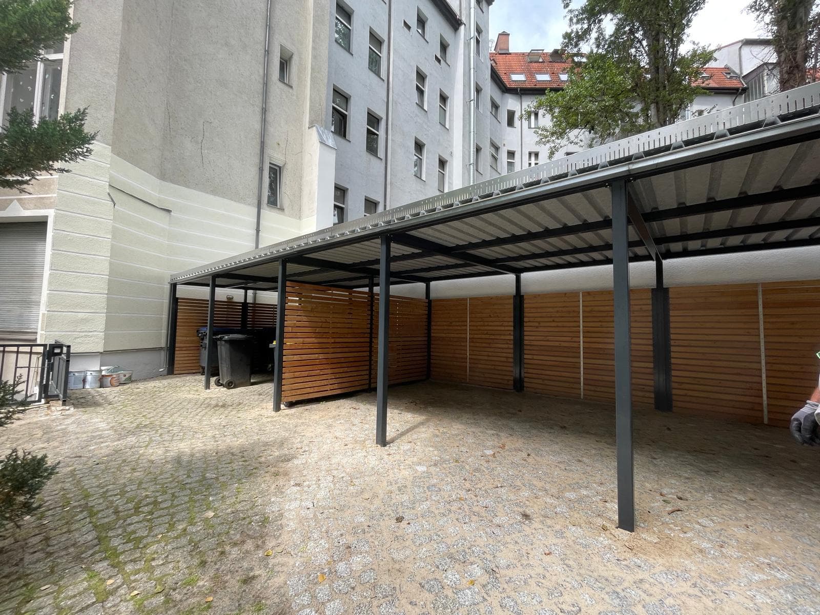 Von Sonne und Grün montierte Stahl-Überdachung mit Holzlatten-Sichtschutz in einem Berliner Innenhof